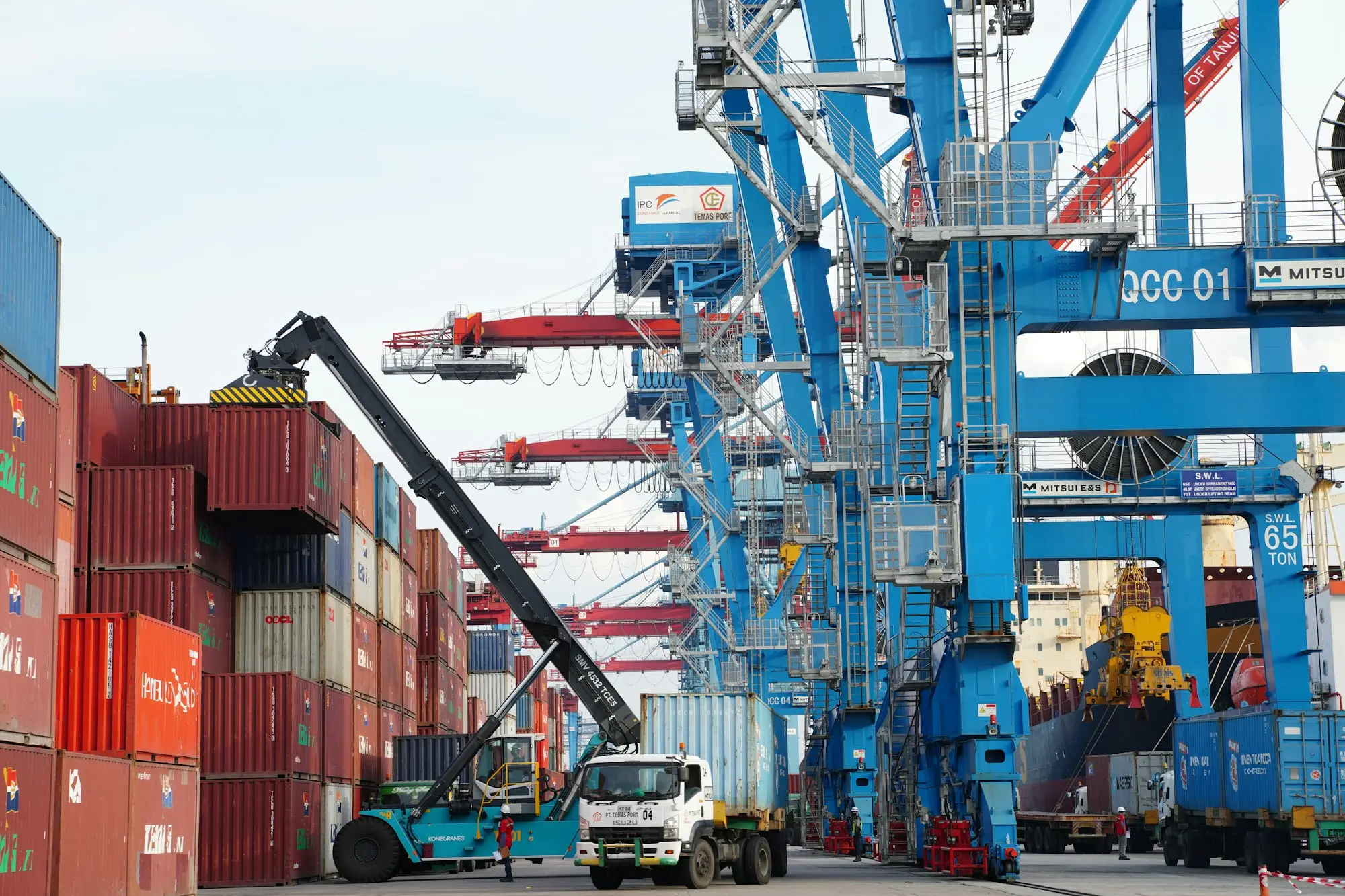 Forklift unloading a container beneath port cranes