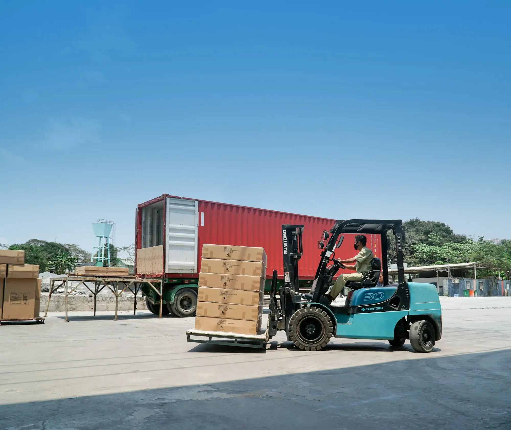 Forklift moving export pallets beside a shipping container