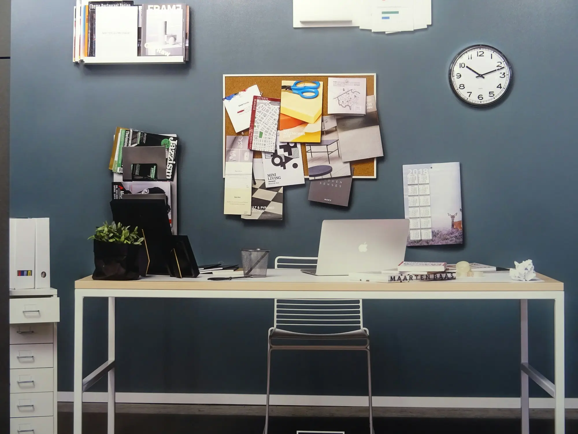 Office wall with a planner, clock and pinboard above a desk